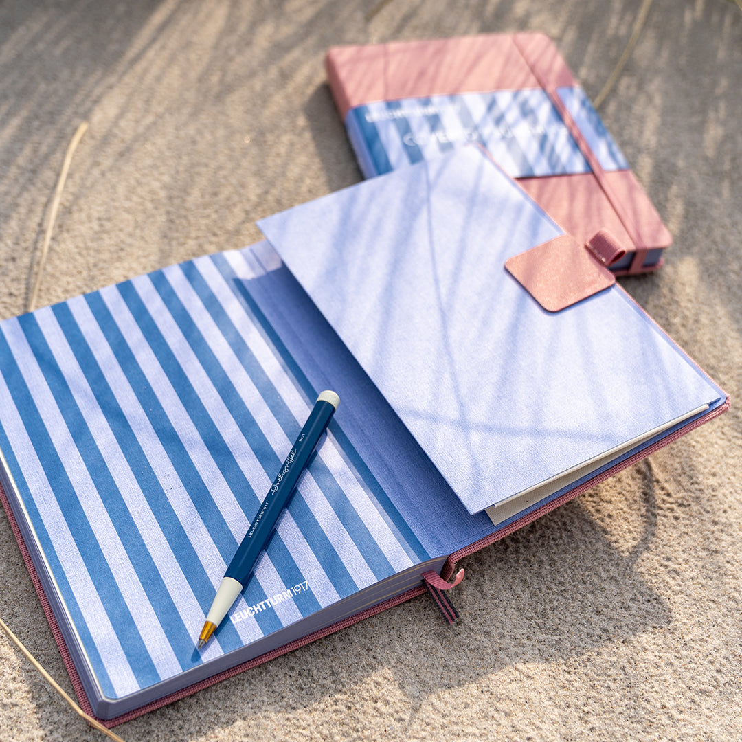 Open notebook with blue and white striped cover and pink interior on a wooden surface.