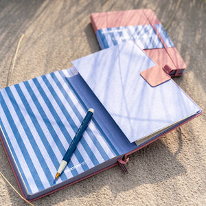 Open notebook with blue and white striped cover and pink interior on a wooden surface.