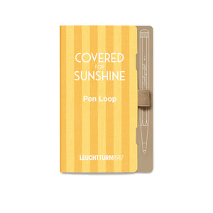 A Leuchtturm1917 pen loop notebook cover in a warm yellow and orange striped pattern, featuring white text that reads 'COVERED FOR SUNSHINE' and 'Pen Loop', with a beige pen loop partially visible on the right side.