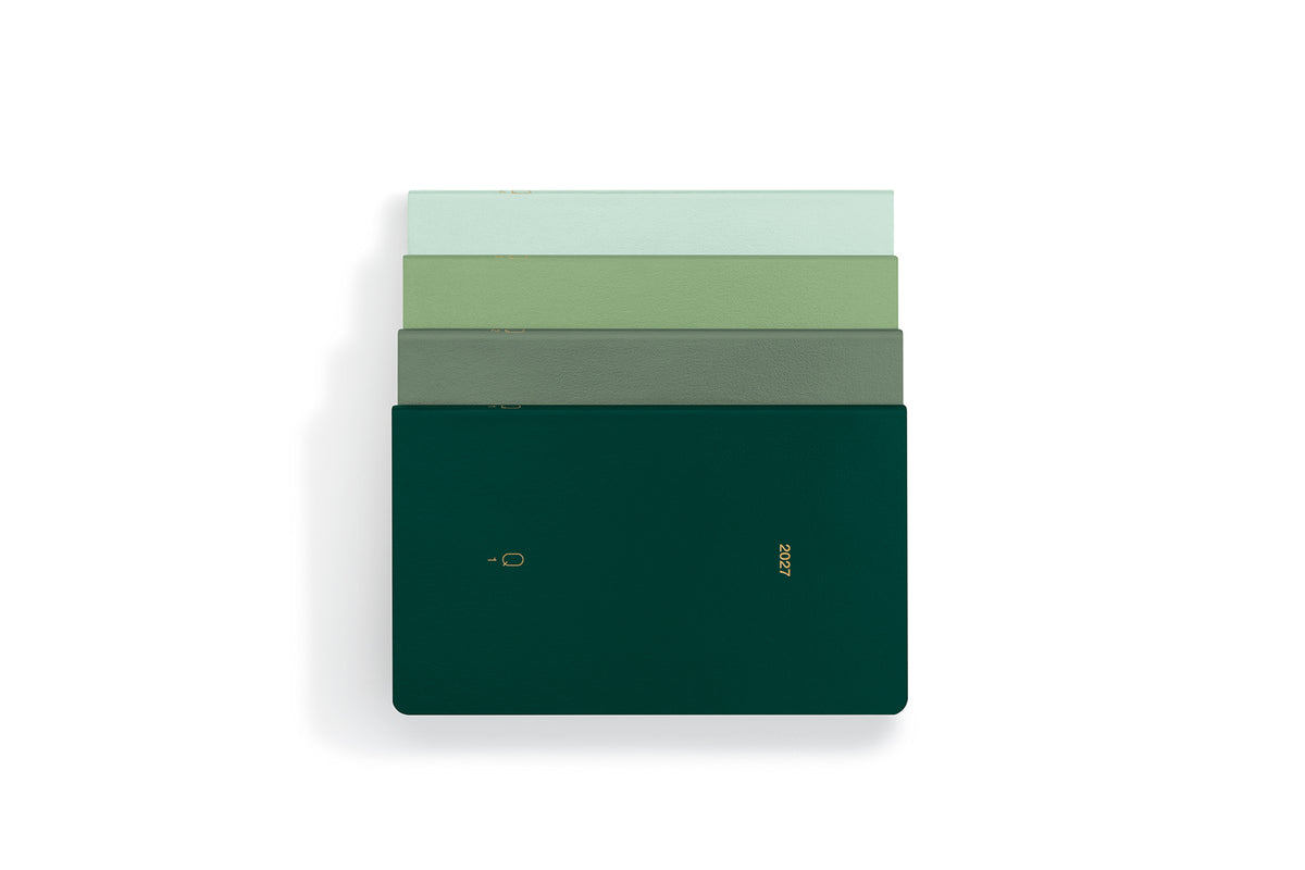A stack of four slim rectangular notebooks or journals in shades of green, with the top two in pale green and the bottom two in darker green, including a dark forest green cover with gold foil text and logo, set against a plain white background.