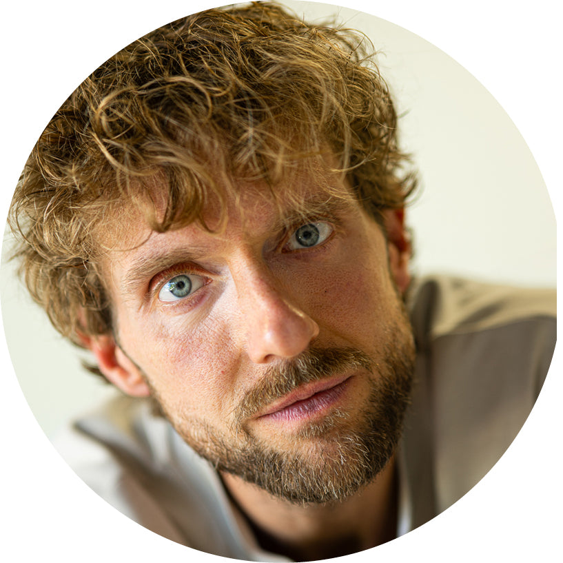 Close-up of a person with wavy hair and beard, wearing a gray shirt.