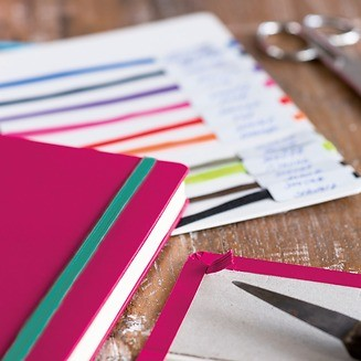 Pink notebook with colorful ribbons on a wooden surface with scissors and paper.