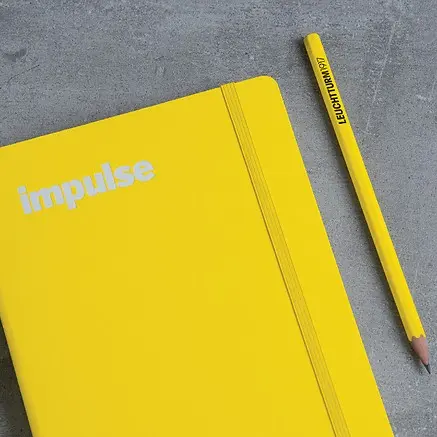 Yellow notebook with 'impulse' text and a yellow pencil on a gray surface