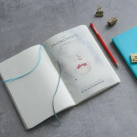 Open notebook with a bookmark on a gray surface with stationery items.