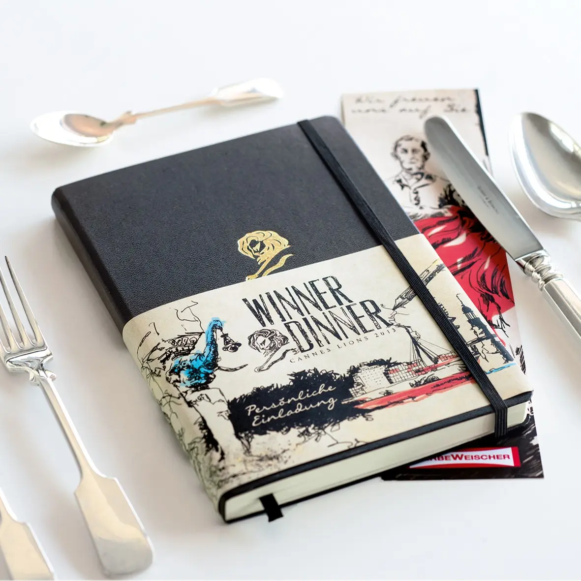 Notebook with artistic cover design on a white surface with cutlery