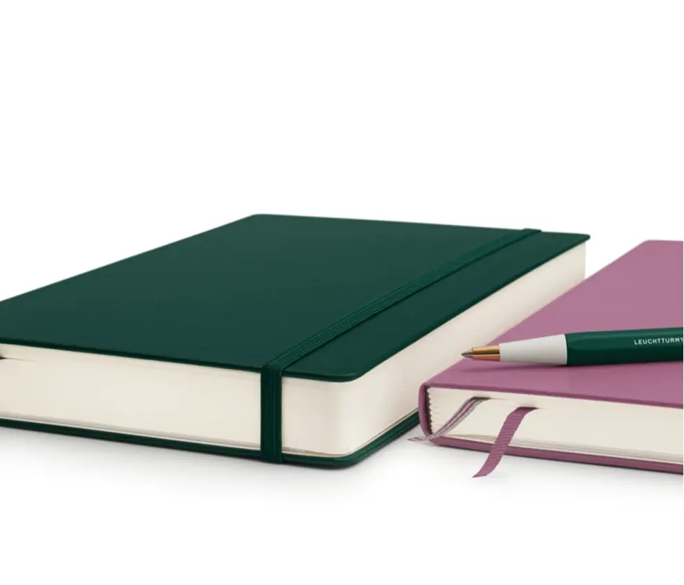 Green notebook and pink notebook with a pen on a white background