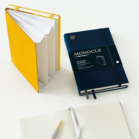 Yellow notebook, blue Monocle notebook, and pen on a white background