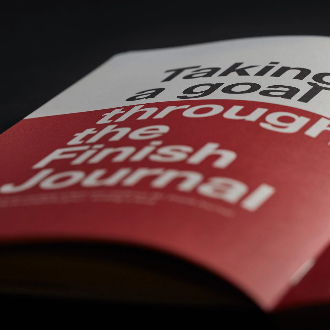Red book titled 'Taking a Goal through the Finish Journal' on a dark background