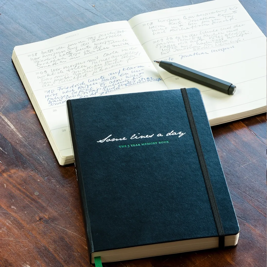 Blue memory book with a pen on an open notebook on a wooden surface