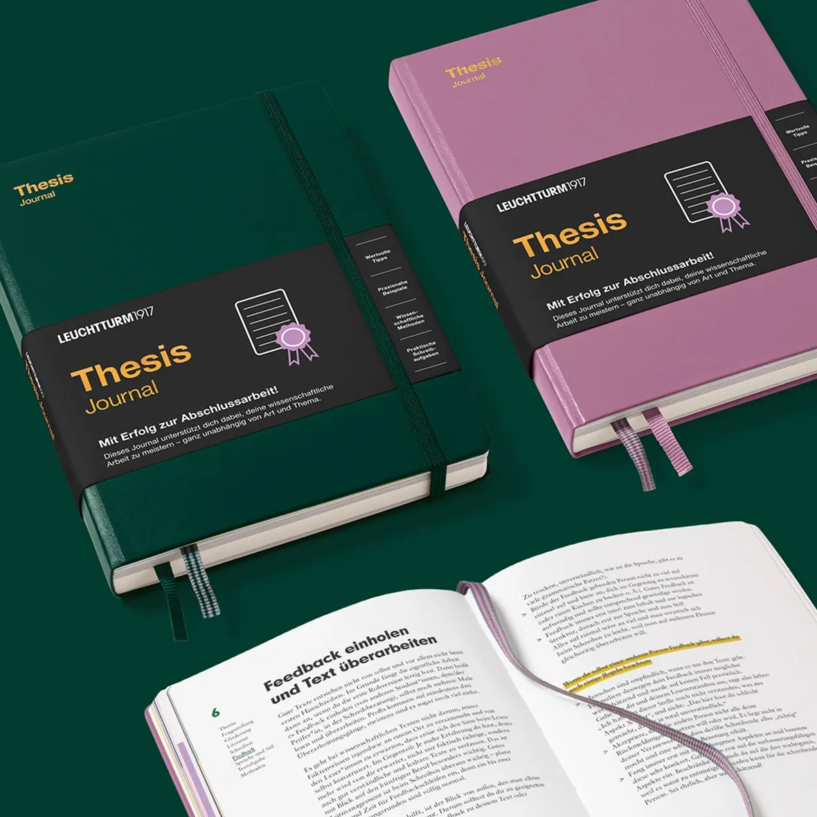 Two thesis journals, one green and one pink, with open book showing text on a green background.