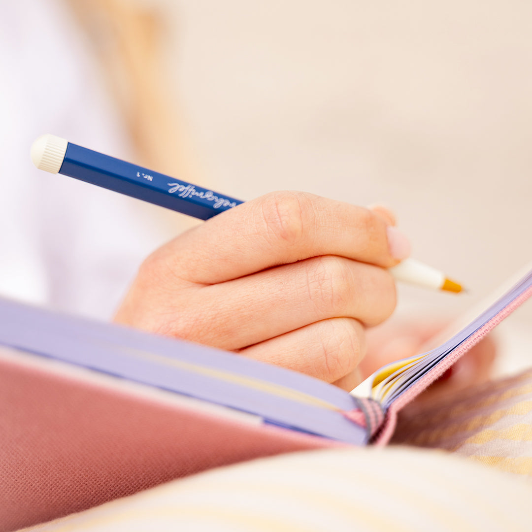 Hand holding a pen with a visible brand logo, writing in a notebook.