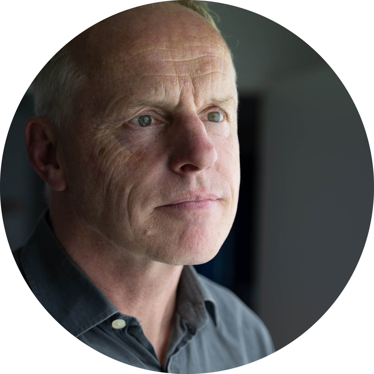 Round profile photo of a man with a neutral expression on a dark background