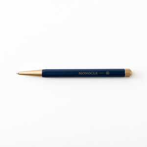 Blue pen with gold accents on a white background, featuring the Monocle logo.