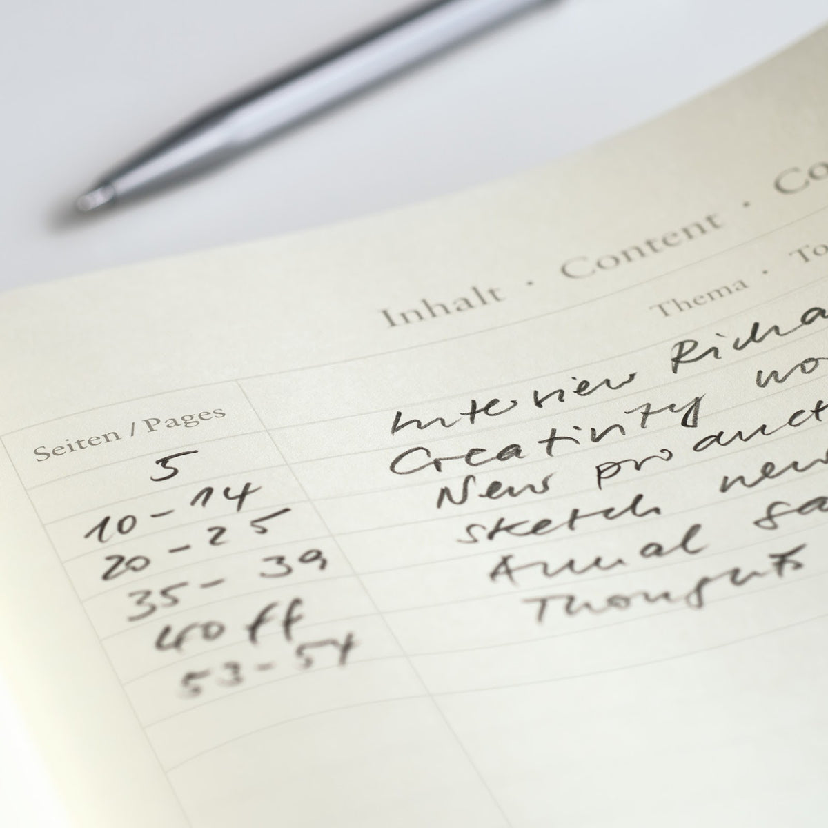 Notebook page with handwritten text and a pen on a white surface
