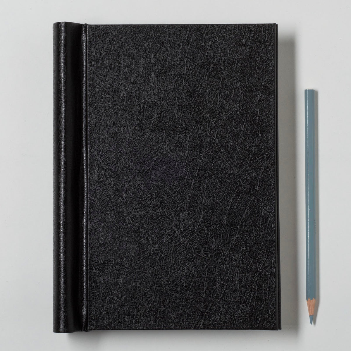 Black leather notebook with a pencil on a light gray background