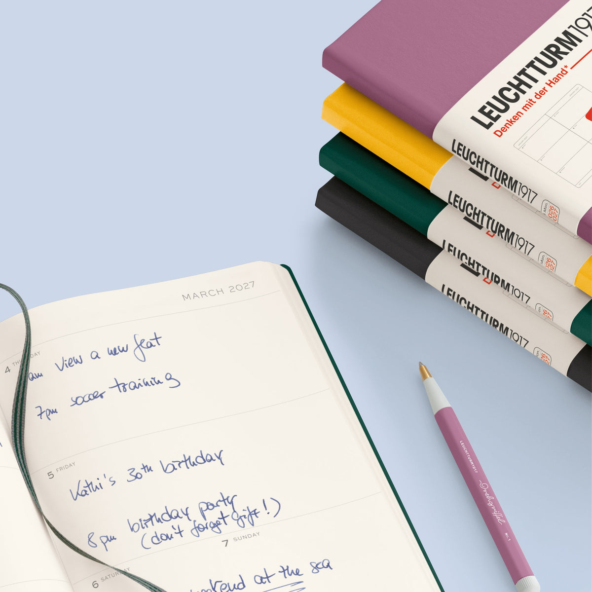 Open notebook with handwritten notes, pen, and stacked Leuchtturm1917 notebooks on a light blue background