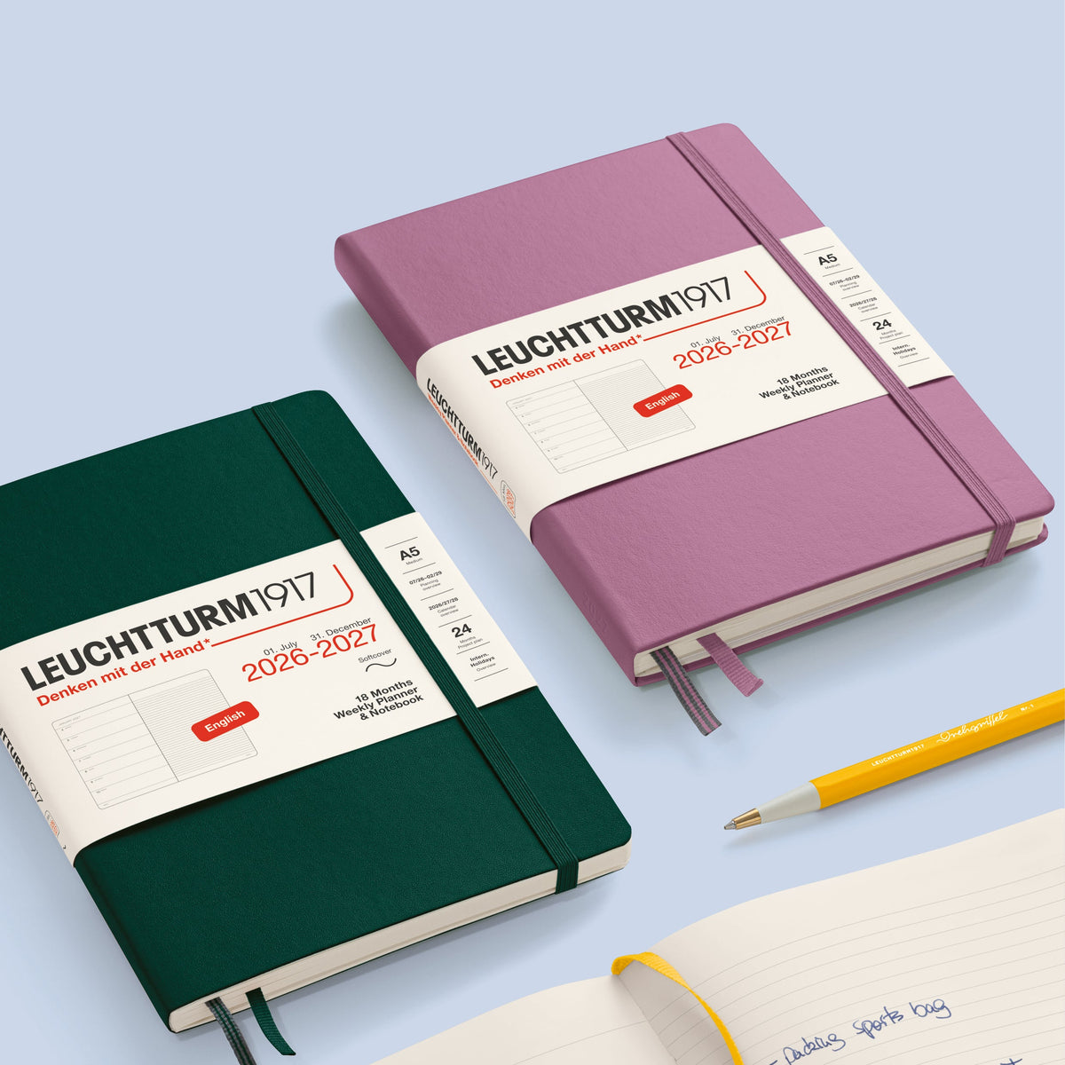 Two Leuchtturm1917 notebooks, one green and one pink, on a light blue background with a pen.