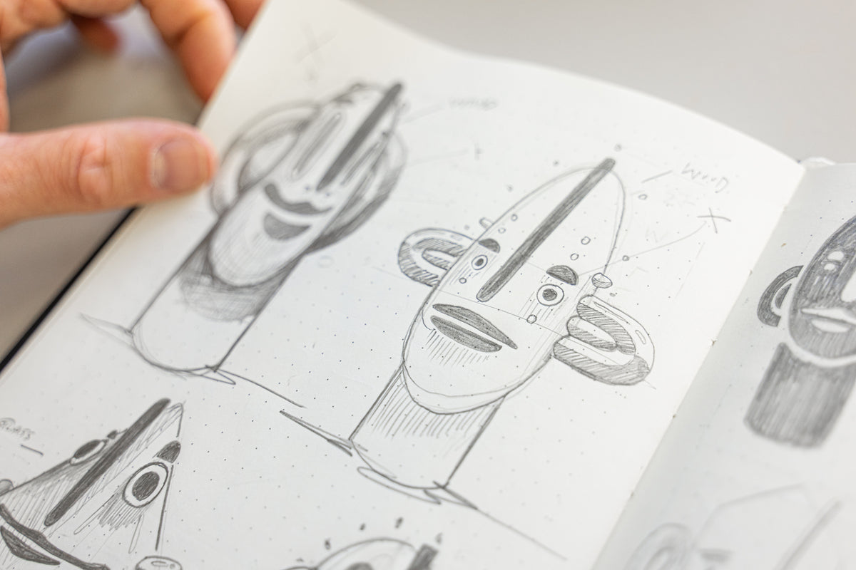 Hand holding a book open to pages with sketches of alien heads.