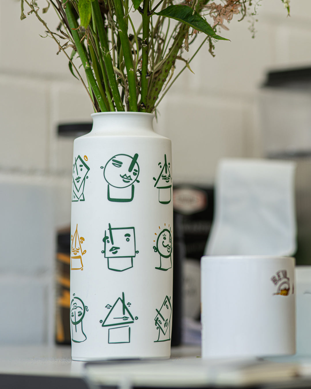 White vase with black and green line art on a table with a blurred background