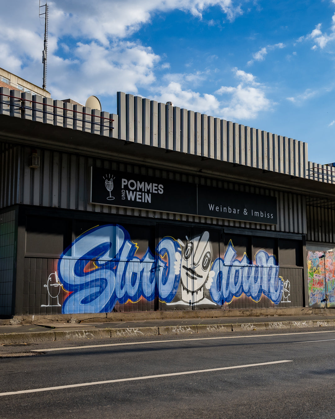 Building with 'Pommes & Wein' sign and graffiti art on a clear day.