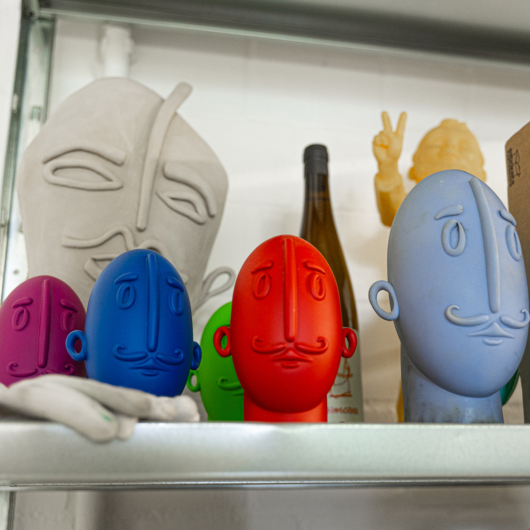 Colorful ceramic face-shaped bottle stoppers on a shelf.