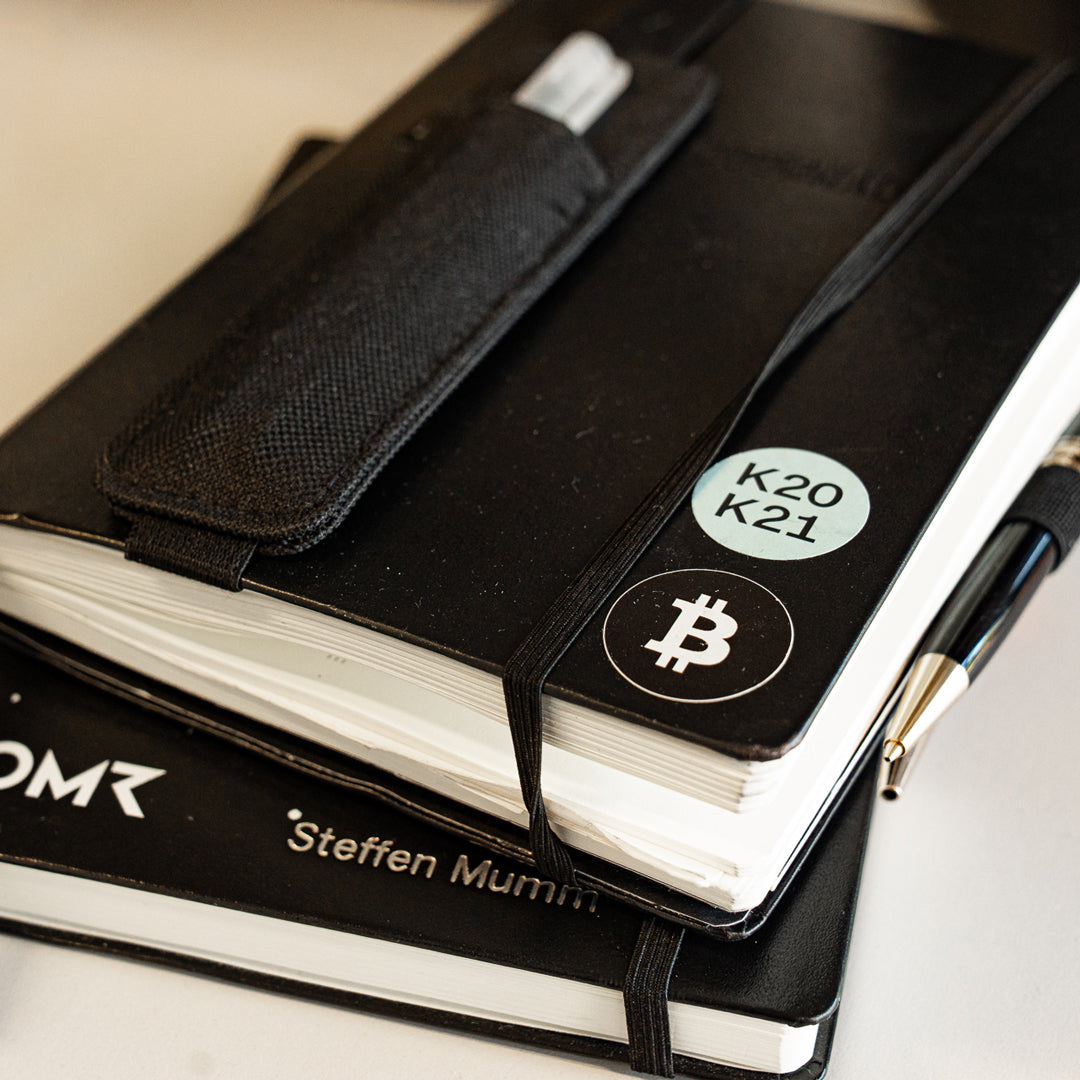 Black notebook with Bitcoin stickers and a pen on a light background