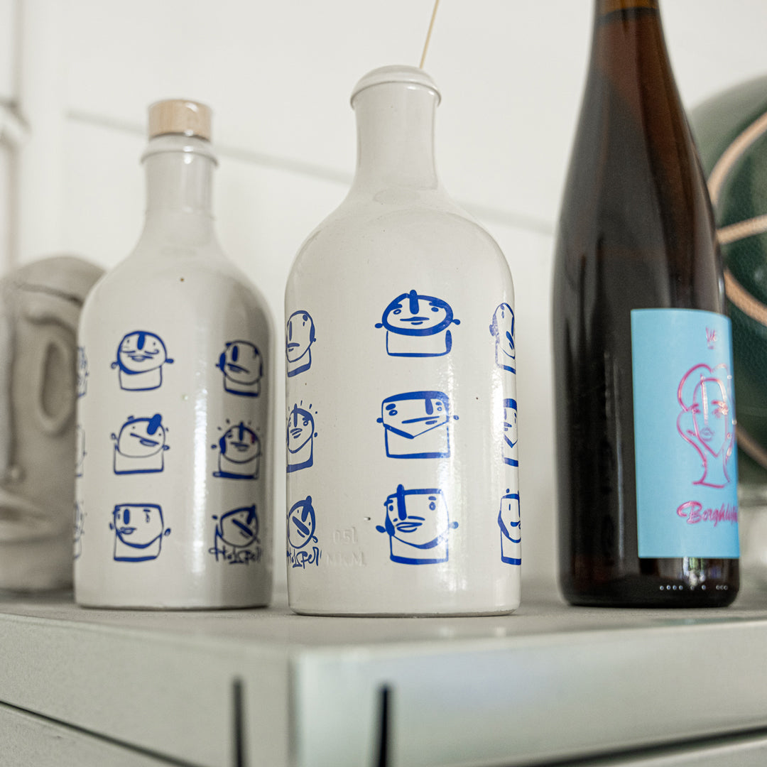 Two white bottles with blue designs on a shelf next to a dark bottle with a colorful label.
