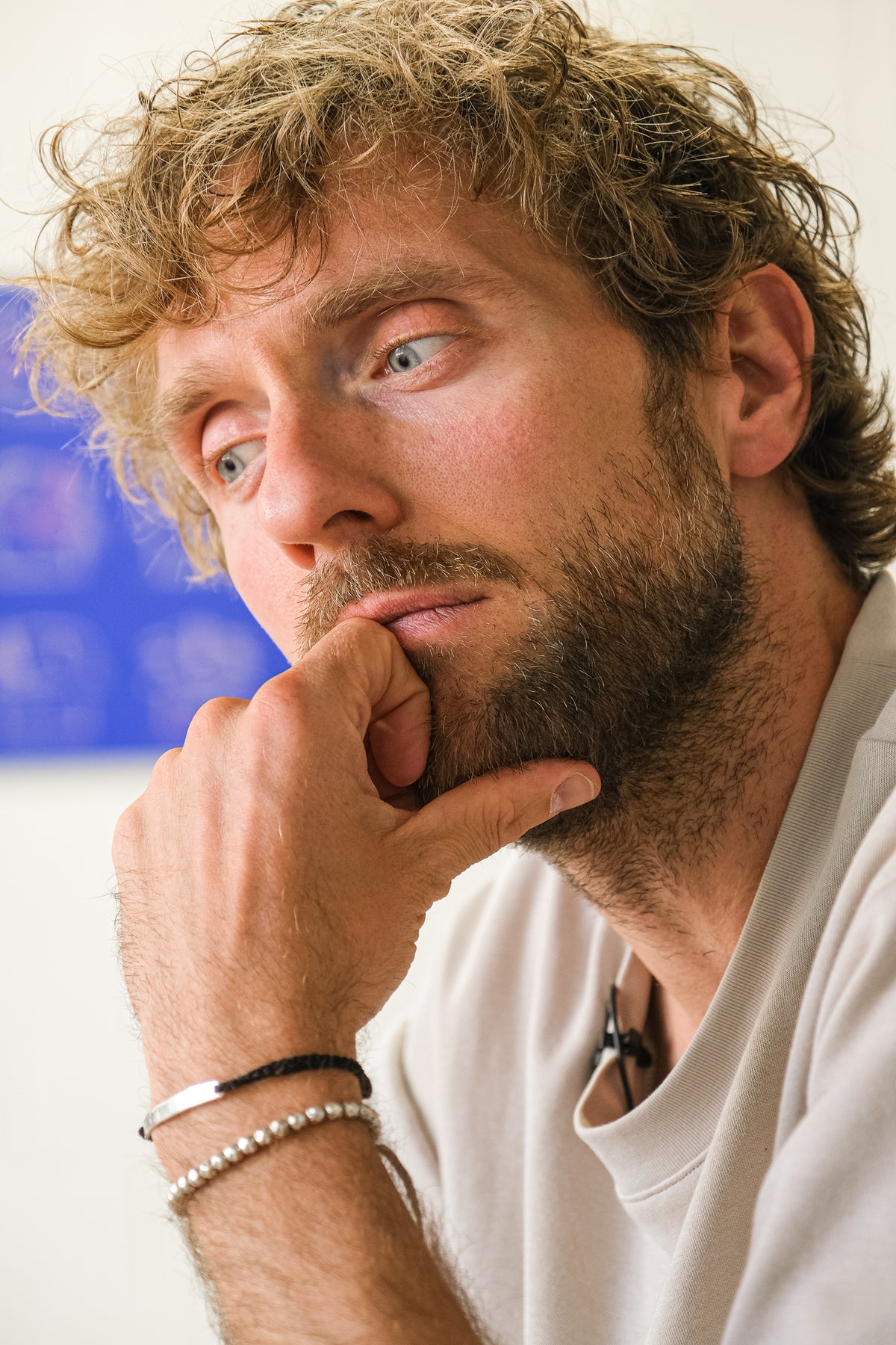 Man with curly hair and beard wearing a white shirt, with a blurred background