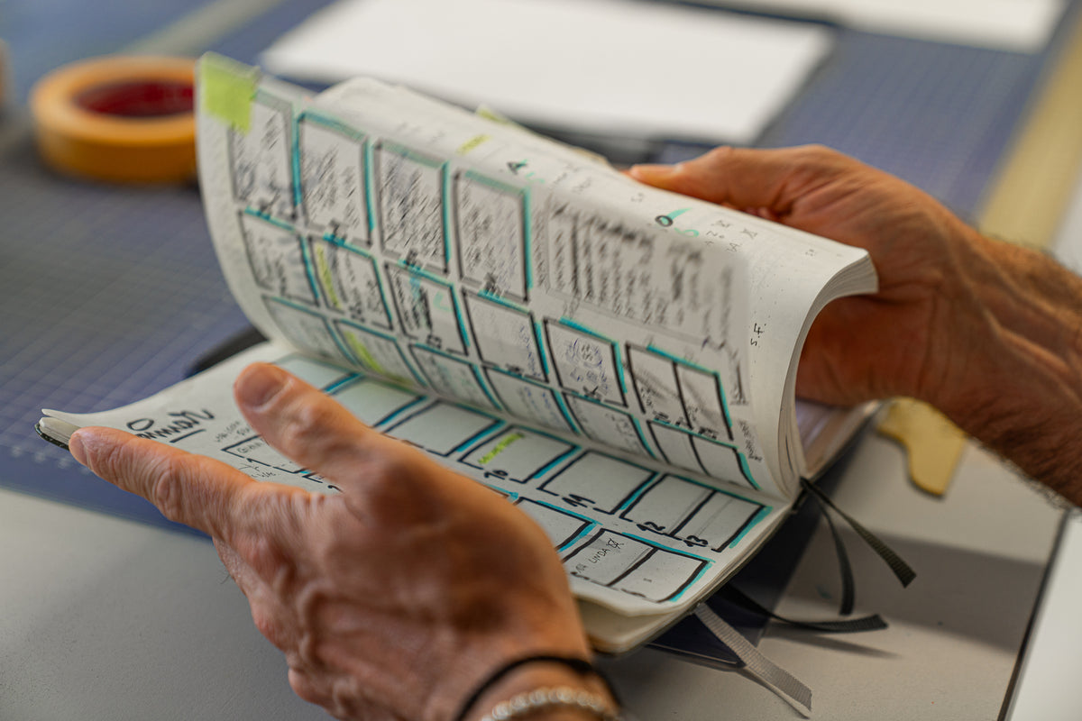 Person holding a book with printed text and pointing at it on a table.
