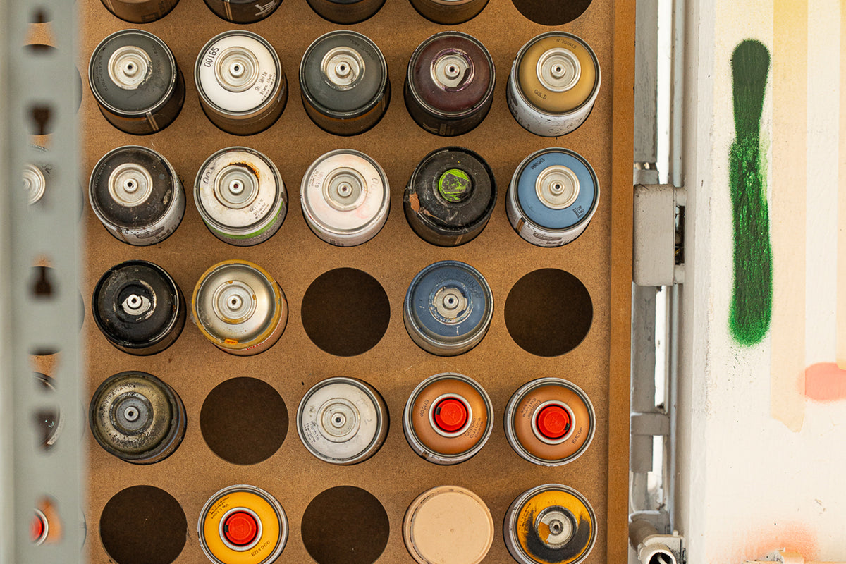 Collection of spray paint cans arranged in a grid on a wooden board.