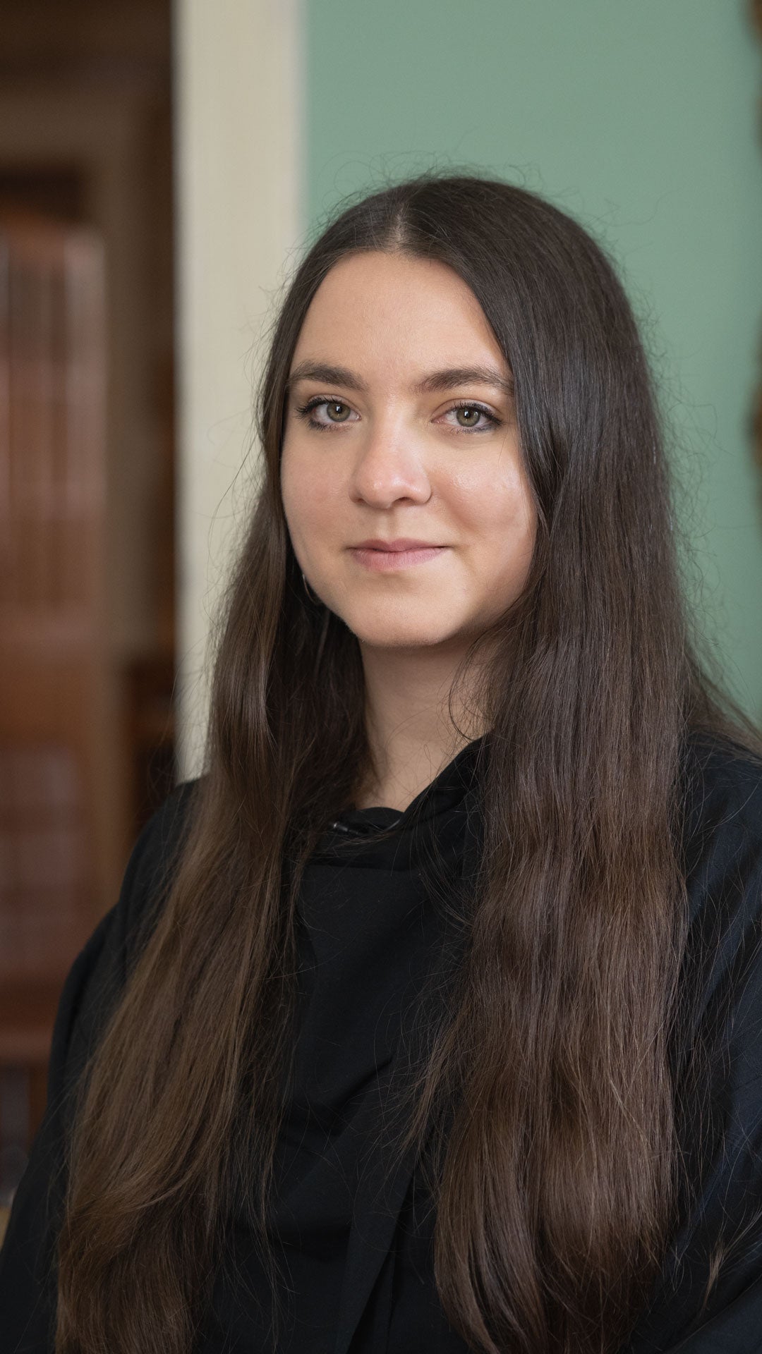 Woman with long brown hair wearing a black top in an indoor setting