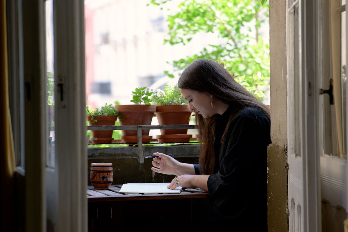 Woman sitting at a table outdoors, surrounded by potted plants.