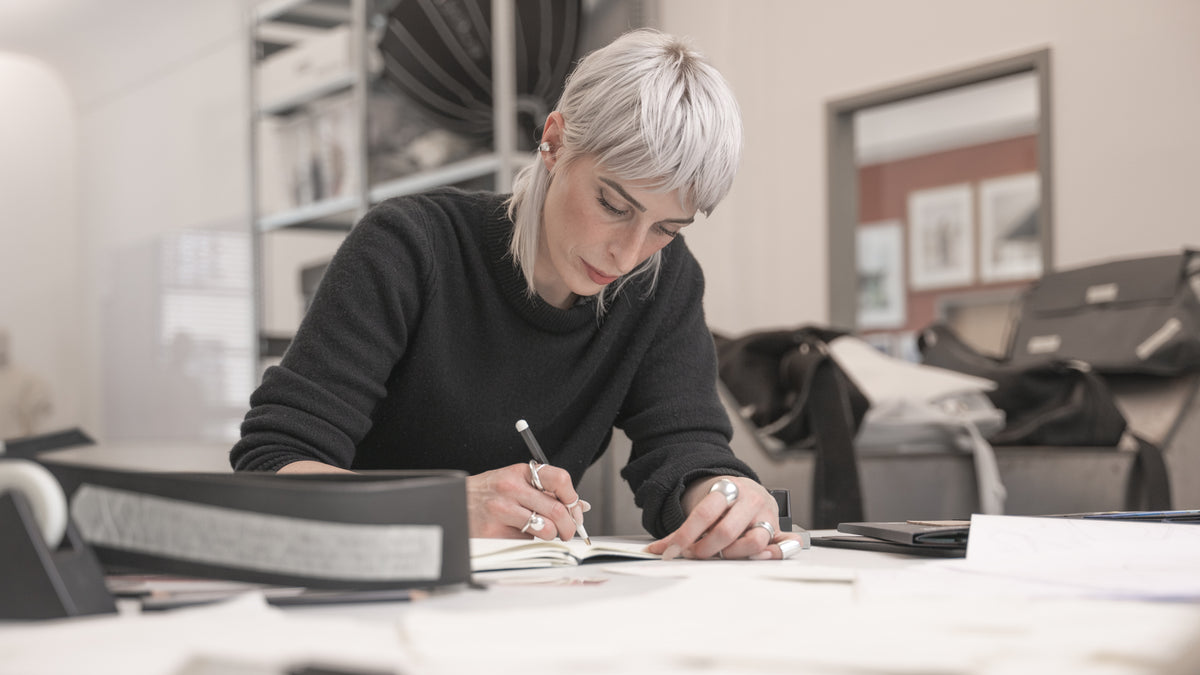 Person sitting at a desk in an office setting, writing in a notebook.