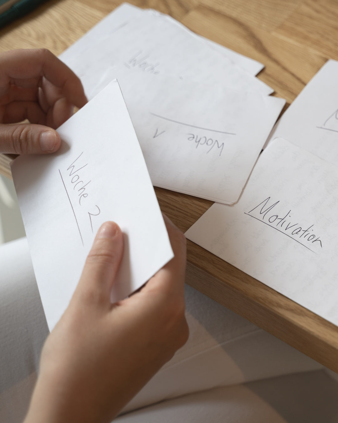 Hands holding a piece of paper with text on it, surrounded by other papers on a wooden surface.
