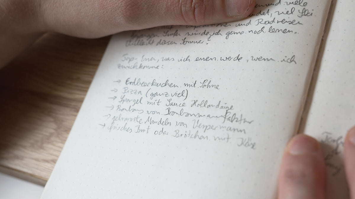 Handwritten text in a notebook held by a person's hands.