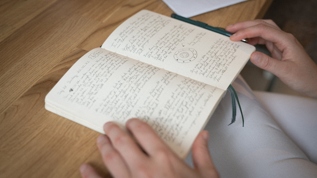 Open book with text on a wooden surface, held by hands