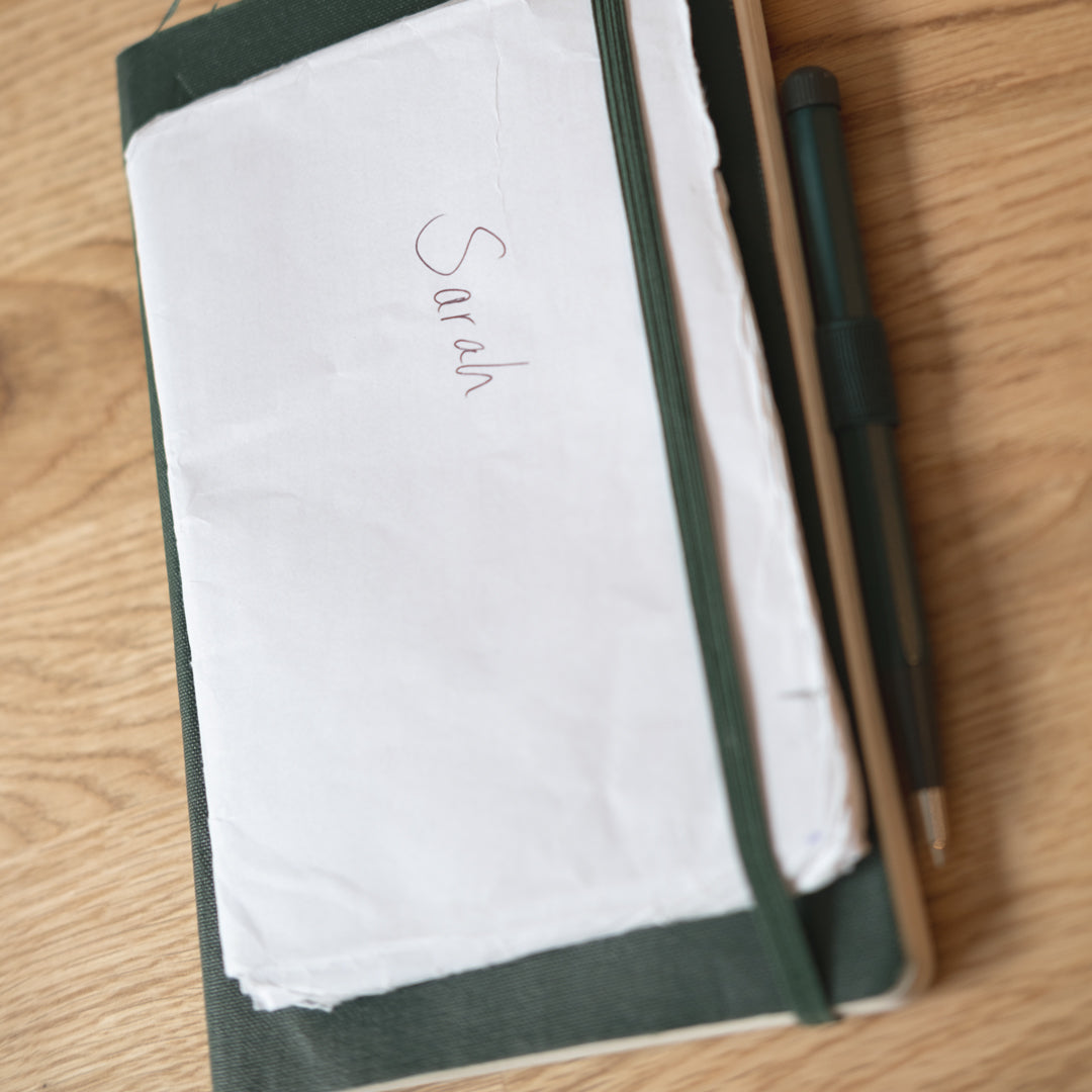 Notebook with a pen on a wooden surface, personalized with 'Sarah'.