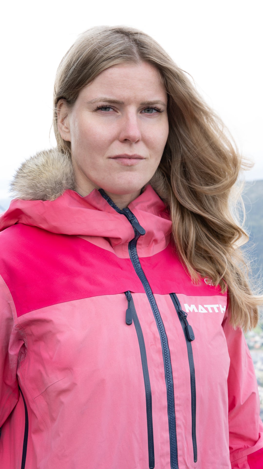Person wearing a pink jacket with a fur-lined hood, standing outdoors.
