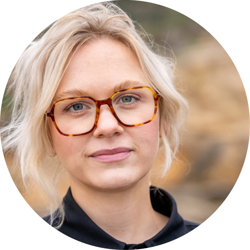 Round profile photo of a person with blonde hair and glasses against a blurred natural background