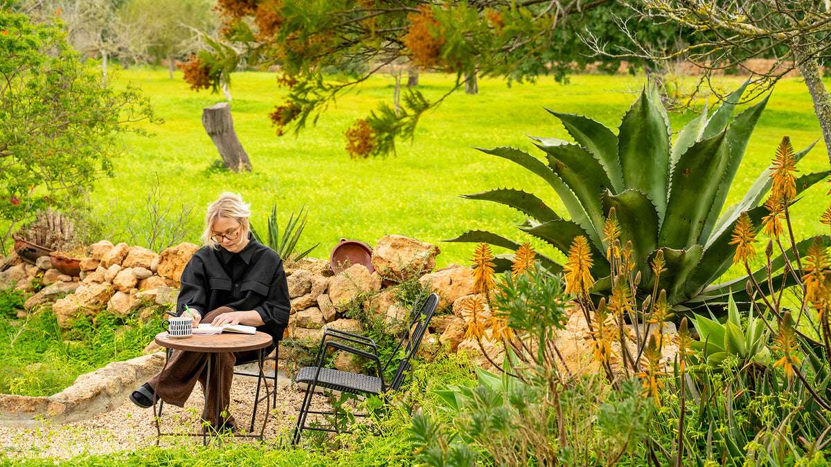 Person sitting at a table in a garden with greenery and plants around