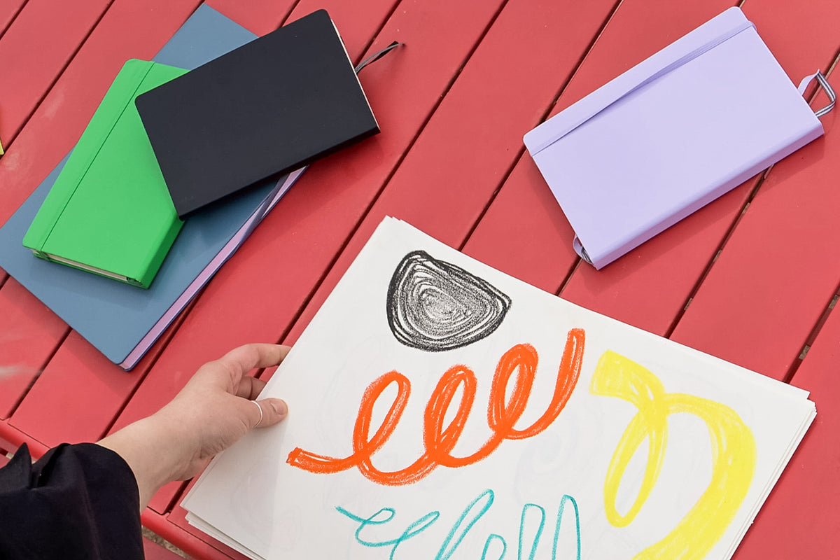 Colorful notebooks and a hand holding a piece of paper with colorful text on a red wooden surface.
