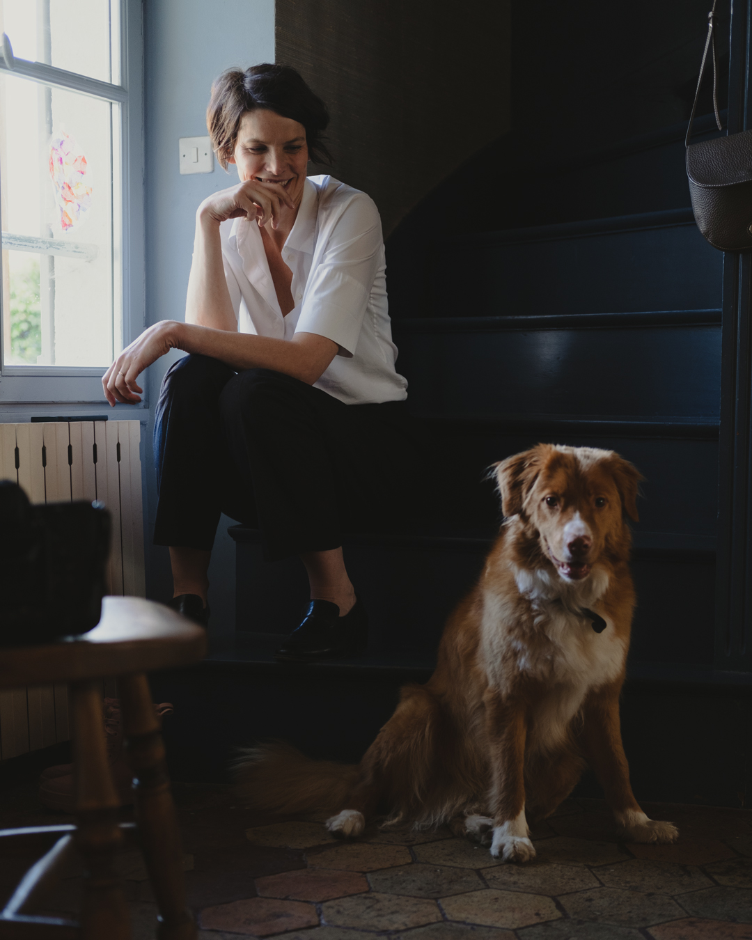 Woman sitting by a window with a dog on a wooden floor.