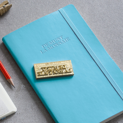 Turquoise notebook with gold embossed text on a gray surface