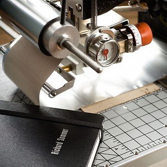 Close-up of a book binding machine in action on a grid surface.