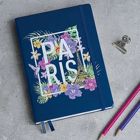 Blue notebook with 'Paris' design on a gray surface with pencils and a clip.