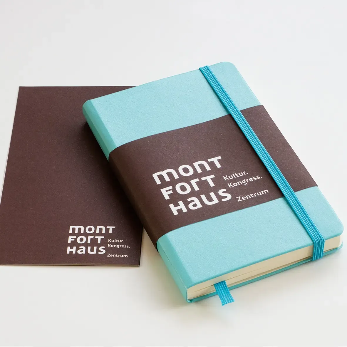 Light blue notebook with a brown band featuring 'mont fort haus' text on a white background