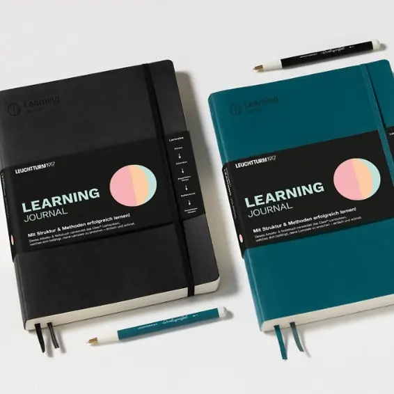 Two 'Learning Journal' books, one black and one teal, with pens on a white background.