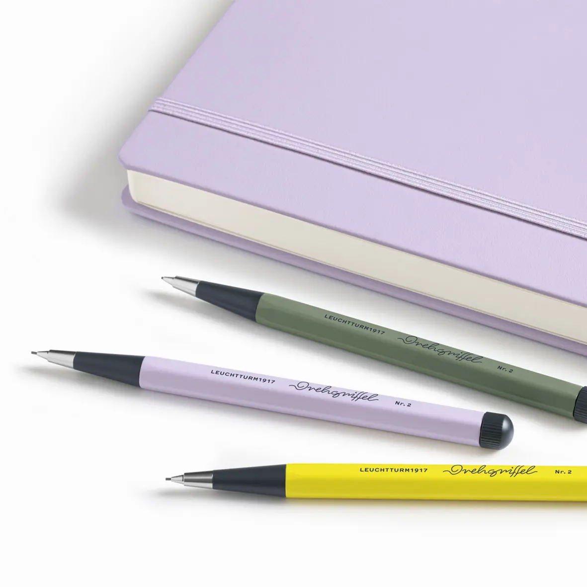 Three pens with different colored barrels on a white surface, with a purple notebook in the background.