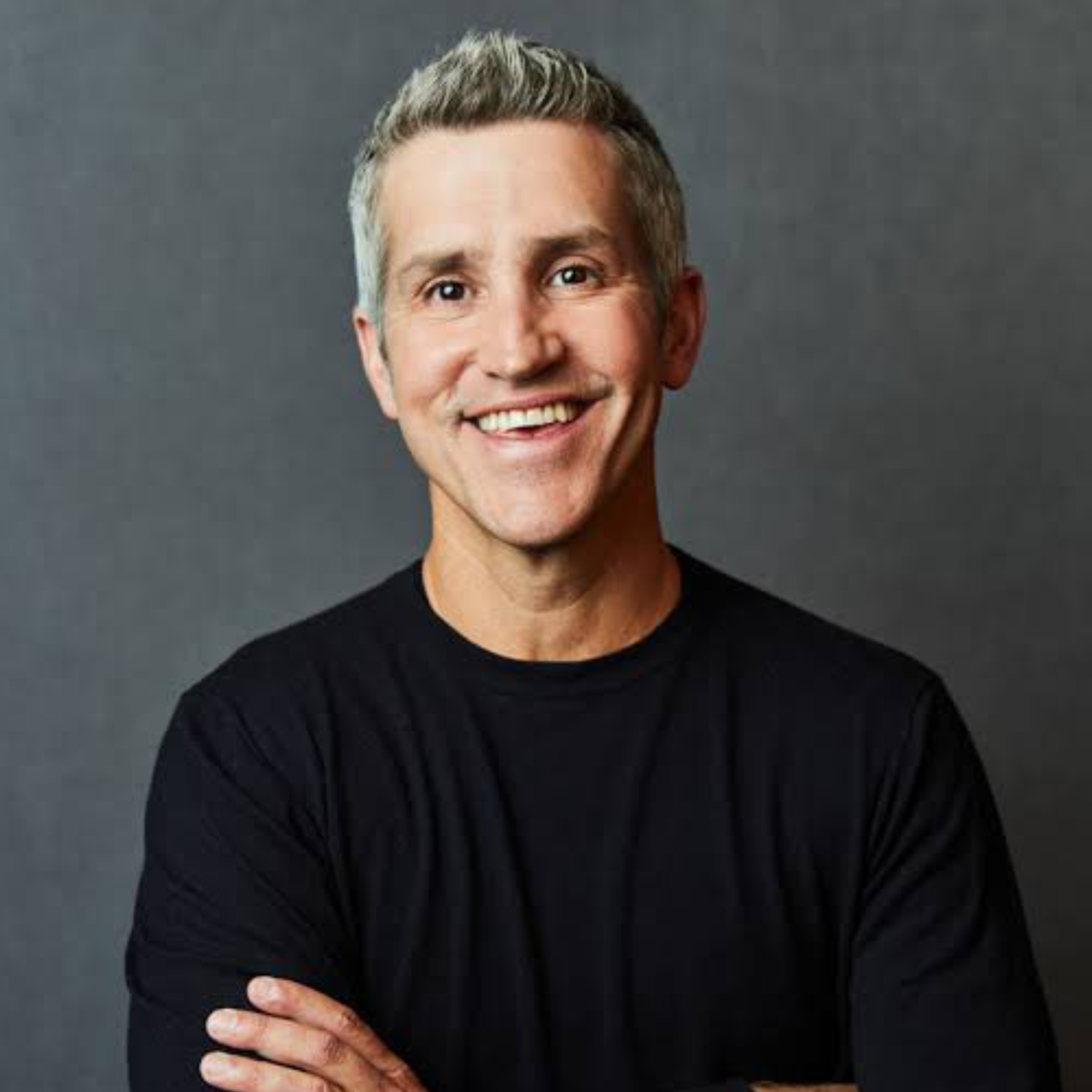 Man with gray hair wearing a black shirt against a dark background