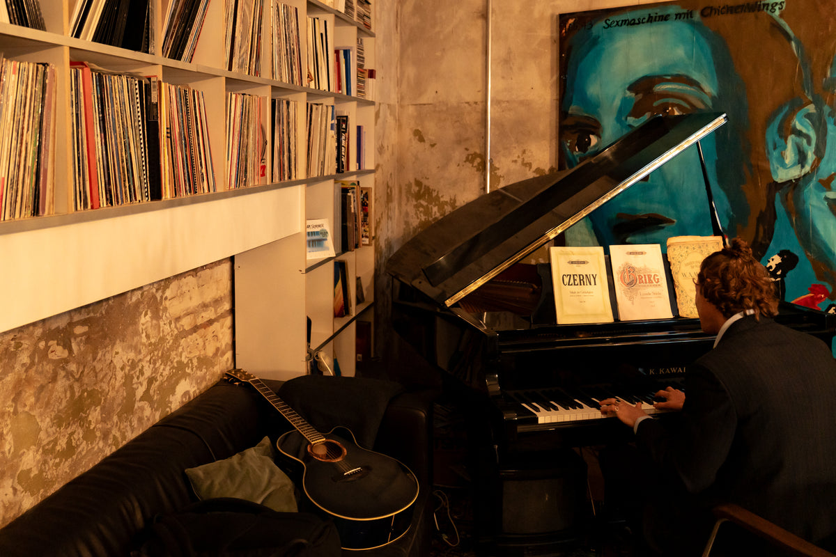 Person playing a piano in a room with bookshelves and a painting on the wall.